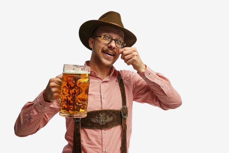 Looks happy. Portrait of attractive young man in hat, wearing folk Bavarian clothes, holding beer mug isolated white background. Alcohol, traditions, holidays, festival and ad concept. Looks happy. Portrait of attractive young man in hat, wearing folk Bavarian clothes, holding beer mug isolated white background. Alcohol, traditions, holidays, festival and ad concept.