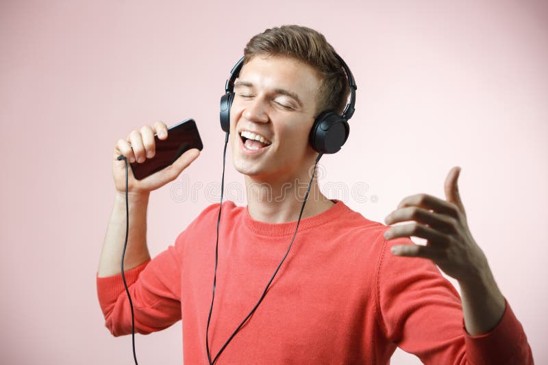 Portrait d'un jeune homme bel avec des écouteurs souriant et écoutant une musique avec un smartphone images stock Portrait d'un jeune homme bel avec des écouteurs souriant et écoutant une musique avec un smartphone images stock