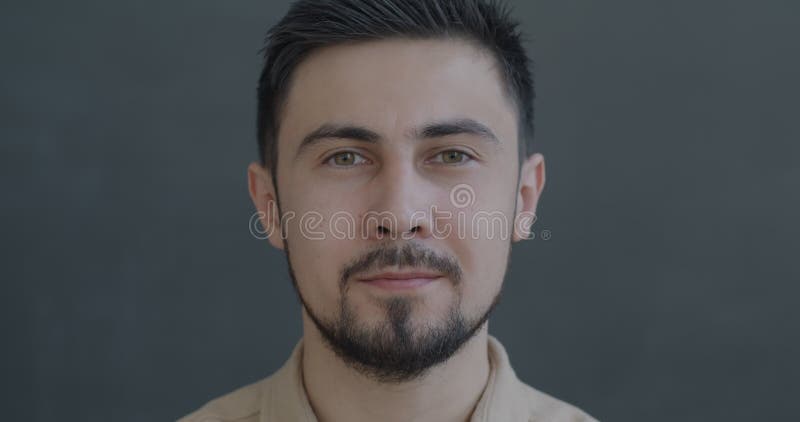 Portrait d'un jeune homme métis sérieux regardant la caméra sans émotion sur fond gris banque de vidéos