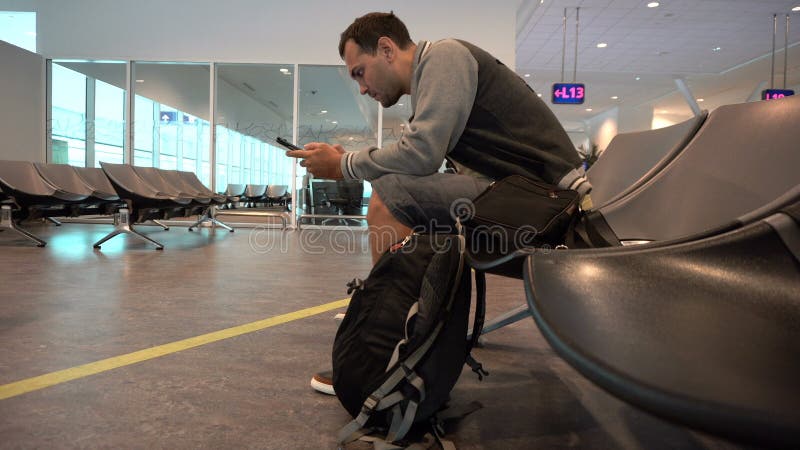 Portrait d'un jeune homme s'asseyant à l'aéroport regardant le comprimé