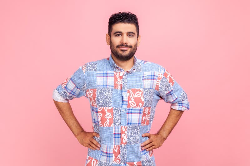 Portrait d'un joli gars barbu joyeux avec le sourire et dans le style décontracté chemise bleue tenant les mains sur les hanches r photo libre de droits