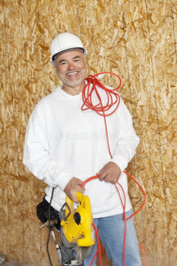 Portrait d'un travailleur de la construction de sexe masculin heureux tenant une scie de puissance et un fil électrique rouge photo libre de droits