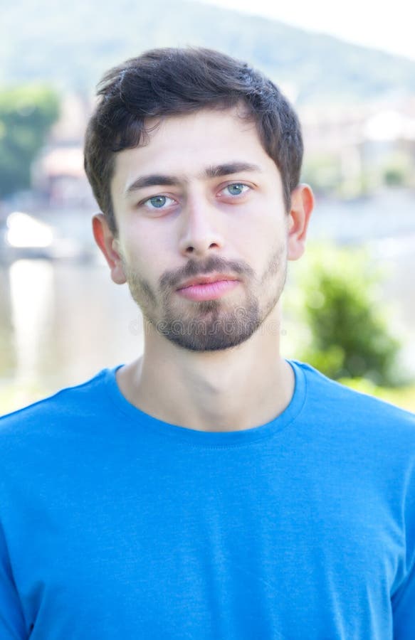 Portrait of a friendly guy with beard outside on a river with meadow and city scape on the background. Portrait of a friendly guy with beard outside on a river with meadow and city scape on the background