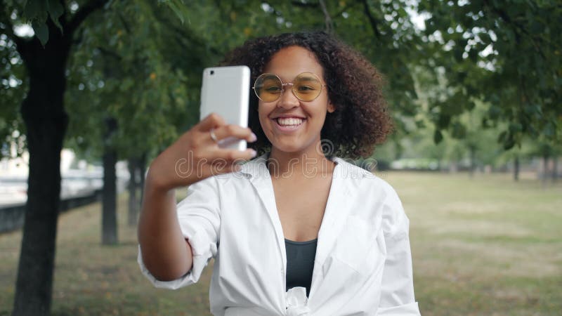 Portrait d'un étudiant afro-américain heureux prenant un selfie à l'extérieur avec son smartphone banque de vidéos