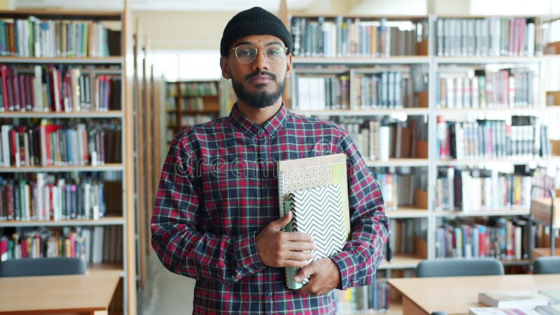Portrait d'un étudiant afro-américain sérieux tenant des livres dans une bibliothèque universitaire clips vidéos