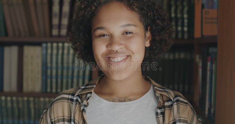 Portrait d'une américaine africaine heureuse debout dans une librairie se tournant vers la caméra souriante clips vidéos