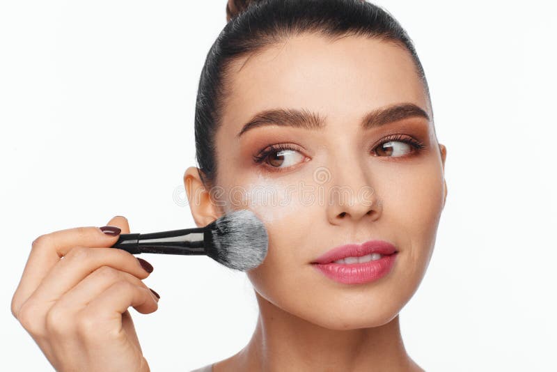 Portrait d'une belle jeune femme tenant une brosse dans sa main et appliquant la poudre à son visage avec une brosse image libre de droits Portrait d'une belle jeune femme tenant une brosse dans sa main et appliquant la poudre à son visage avec une brosse image libre de droits