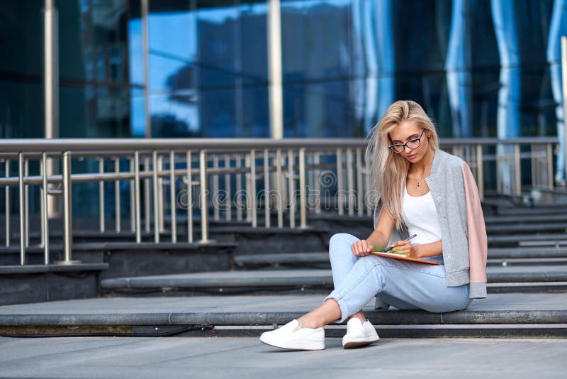 Portrait d'une femme heureuse attirante s'asseyant sur des escaliers ? la rue de ville photographie stock Portrait d'une femme heureuse attirante s'asseyant sur des escaliers ? la rue de ville photographie stock