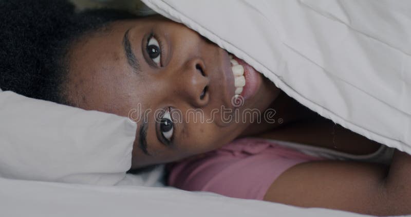 Portrait d'une fille afro-américaine heureuse regardant sous la couverture couchée dans le lit souriant clips vidéos
