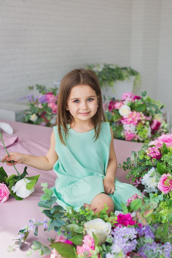 Portrait d'une fille assez petite dans une robe de turquoise près de fleurs dans un studio photographie stock Portrait d'une fille assez petite dans une robe de turquoise près de fleurs dans un studio photographie stock