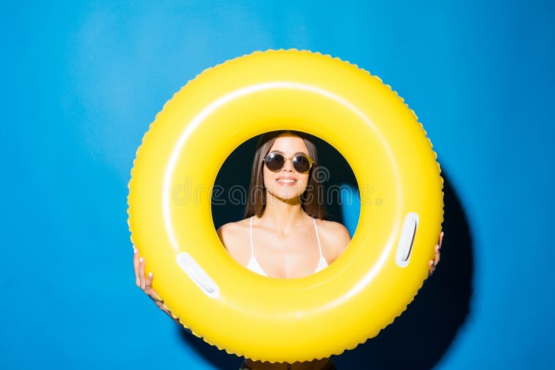Portrait d'une fille heureuse avec des lunettes de soleil habillées dans le maillot de bain regardant par l'anneau gonflable d'is image libre de droits Portrait d'une fille heureuse avec des lunettes de soleil habillées dans le maillot de bain regardant par l'anneau gonflable d'is image libre de droits