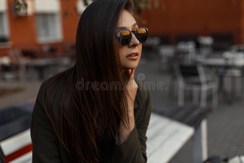 Portrait d'une fille élégante et jeune de brune utilisant un manteau vert et des lunettes de soleil, se reposant dehors image libre de droits Portrait d'une fille élégante et jeune de brune utilisant un manteau vert et des lunettes de soleil, se reposant dehors image libre de droits
