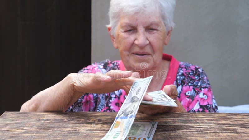 Portrait d'une grand-mère heureuse tenant un paquet d'argent dans les mains et dispersant les devises étrangères sur le bureau. Vi banque de vidéos