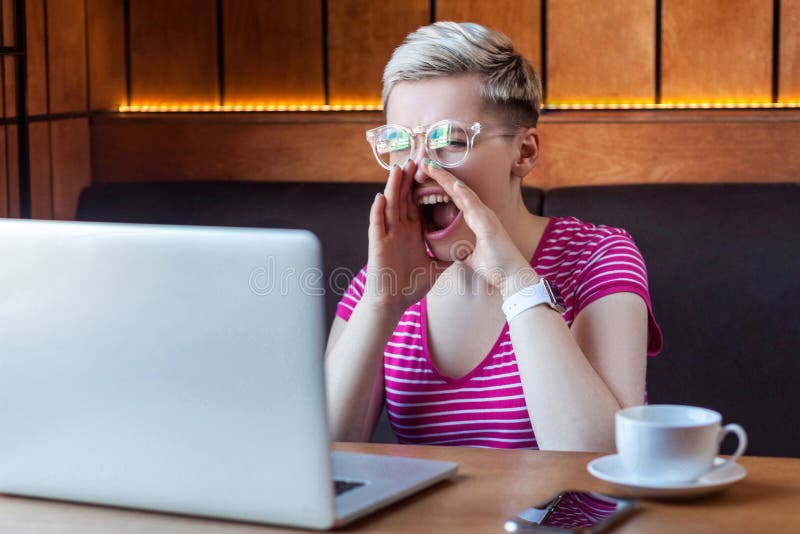Portrait d'une jeune femme adulte en colère avec des cheveux courts blonds, en t-shirt et lunettes roses est assise dans un café images libres de droits