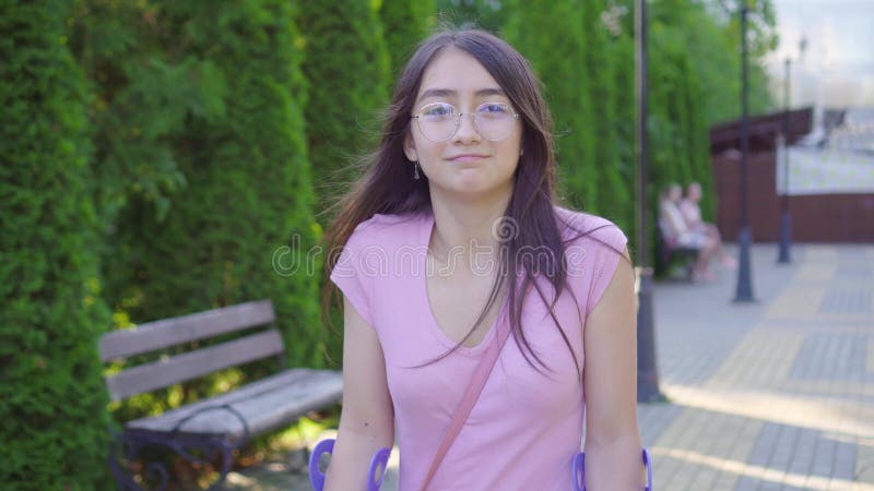 Portrait d'une jeune femme asiatique positive avec une jambe cassée sur des béquilles marchant dans le parc banque de vidéos