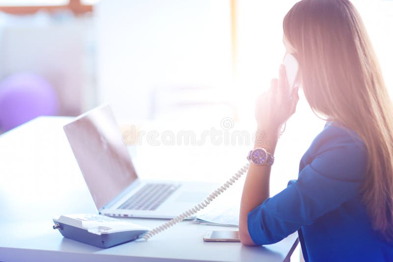 Portrait d'une jeune femme au téléphone devant un ordinateur portable photographie stock libre de droits