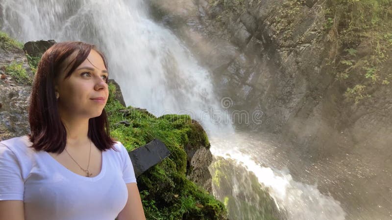 Portrait d'une jeune femme regardant à l'arrière de la cascade. adulte femme touriste bénéficiant d'une belle vue banque de vidéos