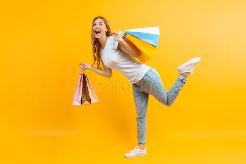 Portrait d'une jeune fille enthousiaste avec des sacs dans des mains, fille heureuse après l'achat sur le fond jaune images stock Portrait d'une jeune fille enthousiaste avec des sacs dans des mains, fille heureuse après l'achat sur le fond jaune images stock