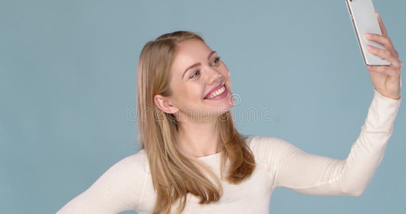 Portrait d'une jeune fille gay avec le sourire adorable prenant le selfie isolé sur le fond bleu.