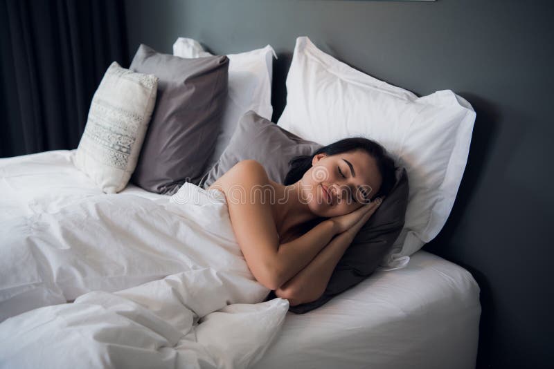 Portrait d'une jeune fille mignonne de brune dormant sur un lit dans le salon léger Sa tête est sur l'oreiller gris et elle est photographie stock libre de droits Portrait d'une jeune fille mignonne de brune dormant sur un lit dans le salon léger Sa tête est sur l'oreiller gris et elle est photographie stock libre de droits