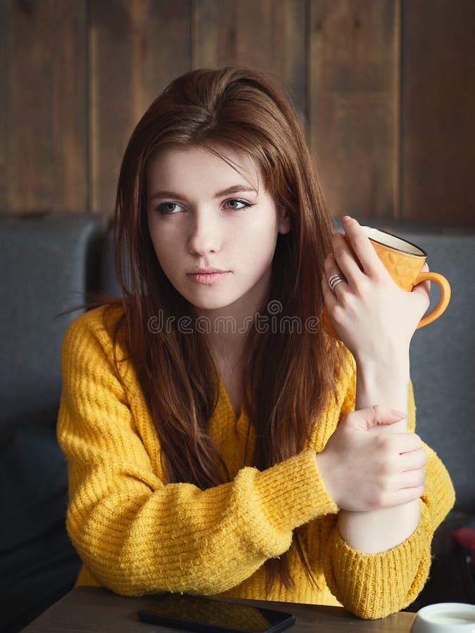 Portrait d'une jolie femme rousse mignonne s'asseyant dans un café appréciant la pause-café de temps libre avec une tasse jaun image stock Portrait d'une jolie femme rousse mignonne s'asseyant dans un café appréciant la pause-café de temps libre avec une tasse jaun image stock