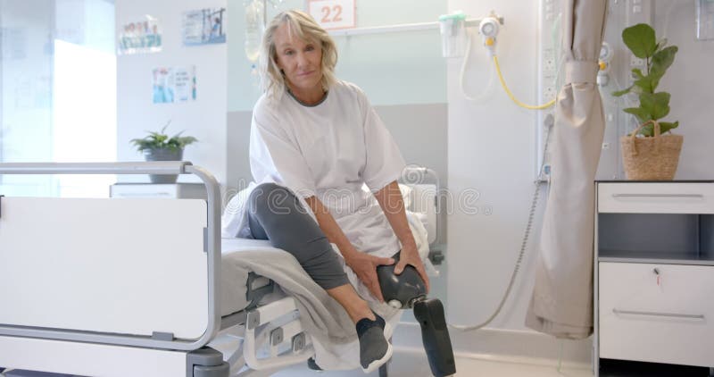 Portrait d'une patiente âgée caucasienne heureuse avec prothèse à la jambe assise dans le lit à l'hôpital