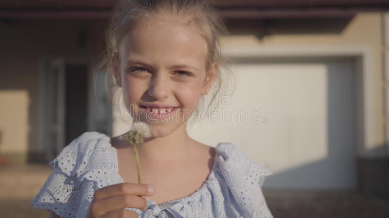 Portrait d'une petite fille assez mignonne soufflant un pissenlit et regardant le sourire de caméra Le temps de dépense d'enfant