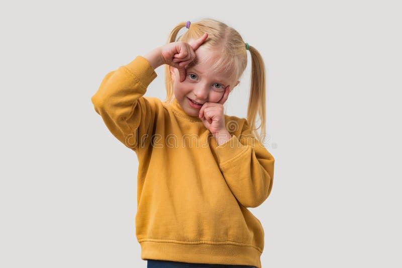 Portrait d'une petite fille aux cheveux blonds dans un pull jaune fait cadre avec ses doigts photo stock