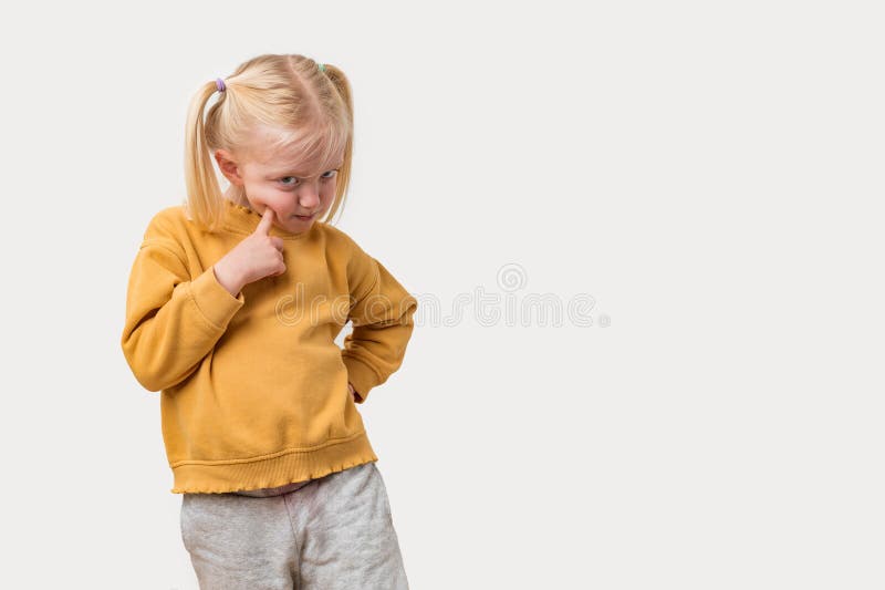 Portrait d'une petite fille aux cheveux blonds dans un pull jaune regardant la caméra avec une expression sérieuse. image libre de droits