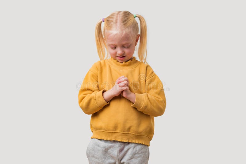 Portrait d'une petite fille de prière timide aux cheveux blonds en chandail jaune sur fond clair photo stock