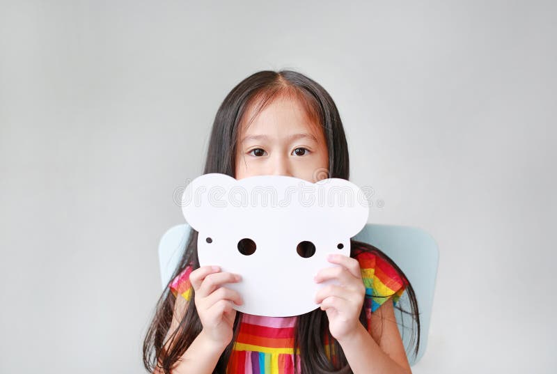 Portrait d'une petite fille tenant un masque blanc blanc en papier blanc sur fond blanc Idée et concept pour image libre de droits Portrait d'une petite fille tenant un masque blanc blanc en papier blanc sur fond blanc Idée et concept pour image libre de droits