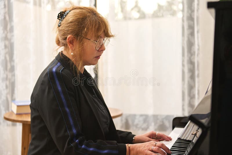 Portrait d'une pianiste mature jouant la mélodie classique sur piano à queue à la maison assise seule au piano noir vintage photographie stock