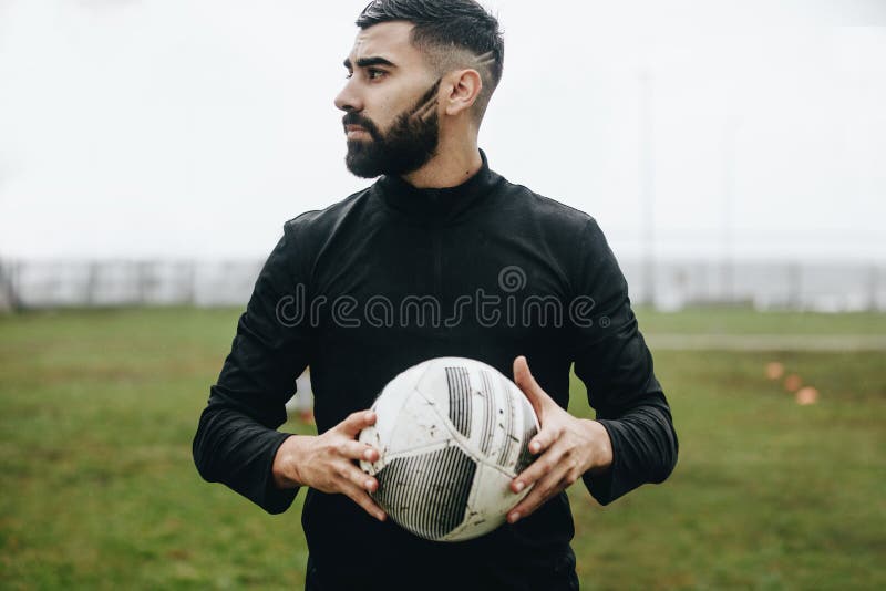 Portrait d'une position de joueur de football sur le champ tenant une boule regardant loin Position de footballeur sur la terre t images stock Portrait d'une position de joueur de football sur le champ tenant une boule regardant loin Position de footballeur sur la terre t images stock