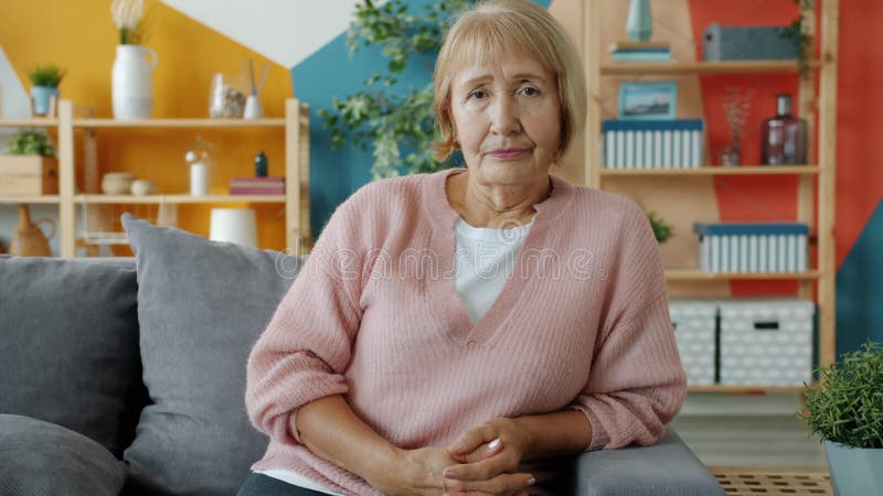 Portrait d'une vieille femme sérieuse avec une coiffure moderne regardant la caméra dans la maison clips vidéos