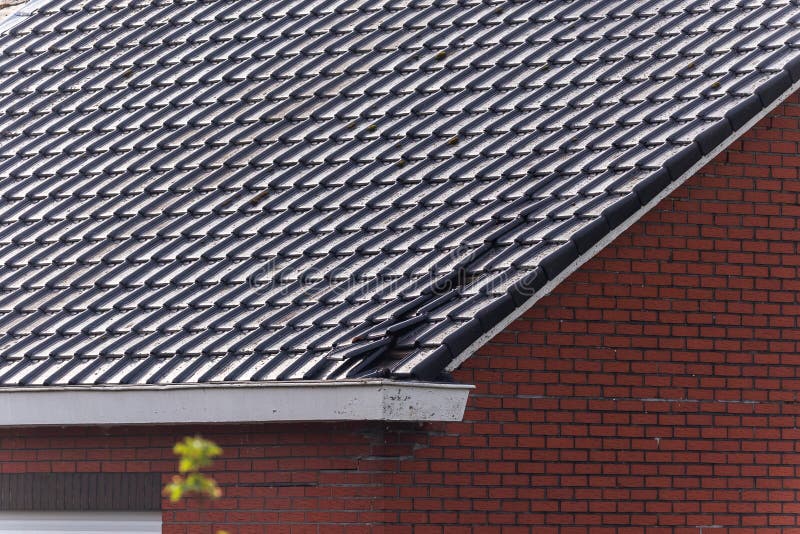 A portrait of a damaged black tile roof of a house. The building got destroyed by a big storm with high wind speeds on the