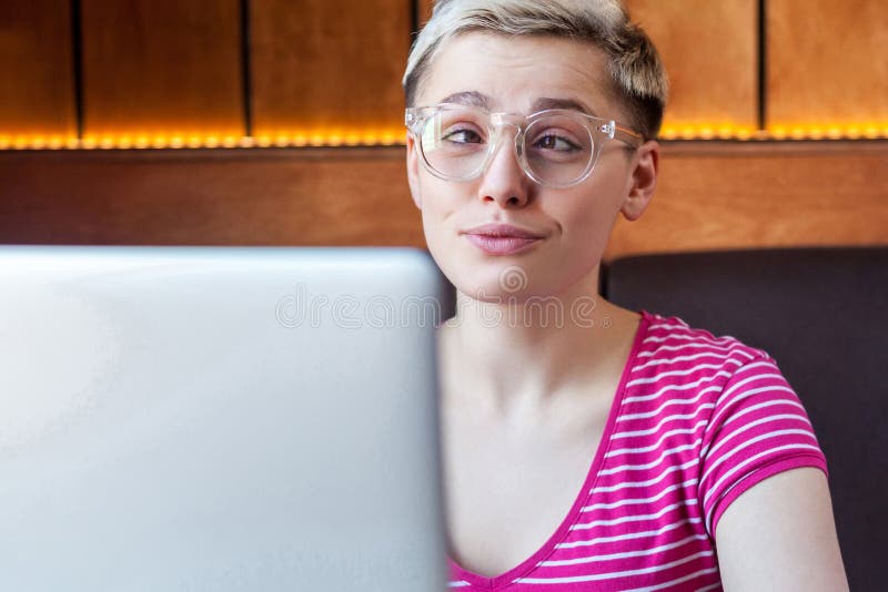 Portrait de clôture d'une jeune fille joyeuse et enfantine aux cheveux courts en t-shirt rose et lunettes est assise dans un café photos stock