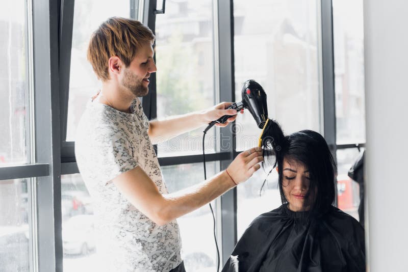 Portrait de coiffeur heureux tenant le peigne et le dessiccateur de coup dans le salon photographie stock Portrait de coiffeur heureux tenant le peigne et le dessiccateur de coup dans le salon photographie stock