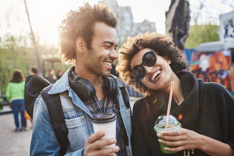 Portrait de deux amants avec des coupes de cheveux Afro, flânant en parc et café potable tout en parlant et appréciant des dépens photos stock Portrait de deux amants avec des coupes de cheveux Afro, flânant en parc et café potable tout en parlant et appréciant des dépens photos stock