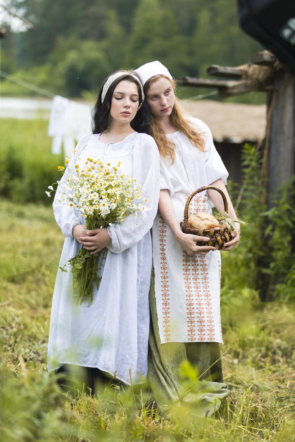 Portrait of Two Beautiful Caucasian Girls Posing Together on Countryside Environment with Camomile Flowers and Basket of Bread. Vertical Image. Portrait of Two Beautiful Caucasian Girls Posing Together on Countryside Environment with Camomile Flowers and Basket of Bread. Vertical Image