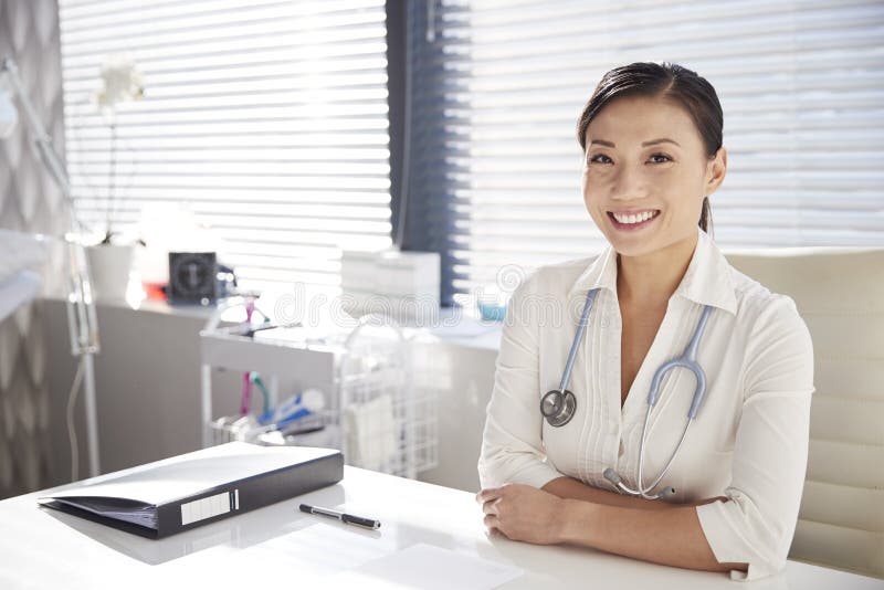 Portrait de docteur féminin de sourire With Stethoscope Sitting derrière le bureau dans le bureau images libres de droits