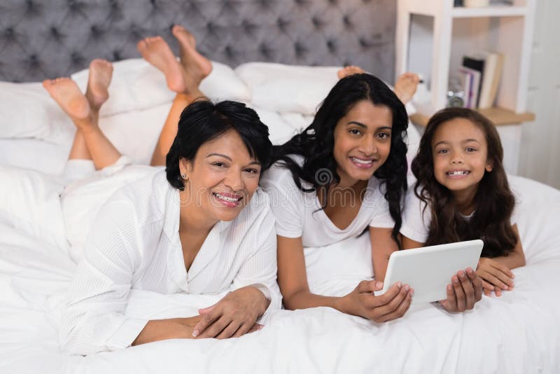 Portrait de famille sur plusieurs générations de sourire utilisant le comprimé numérique tout en se trouvant sur le lit