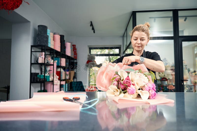 Portrait de femme en tablier tout en créant un bouquet élégant. Portrait d'une femme occupée dans un tablier tout en créant bouquet de fleurs à la mode. fleuriste travaillant dans la boutique fleuriste