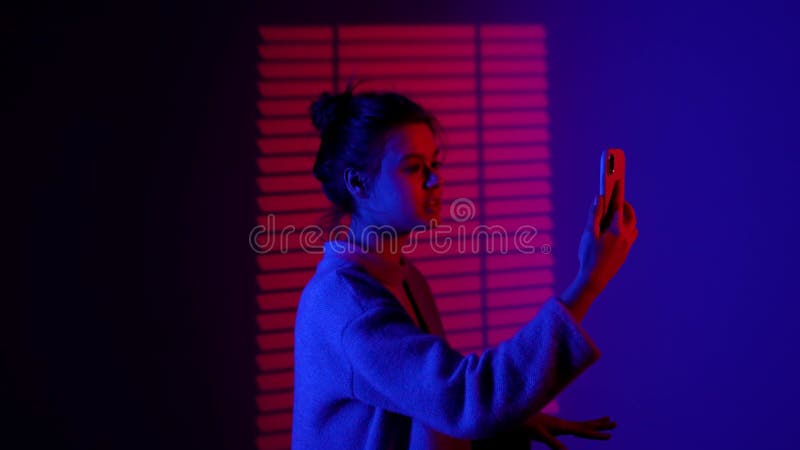 Portrait de femme silhouette en conversation par appel vidéo sur smartphone stand in spolight isolé sur red blue neon studio banque de vidéos