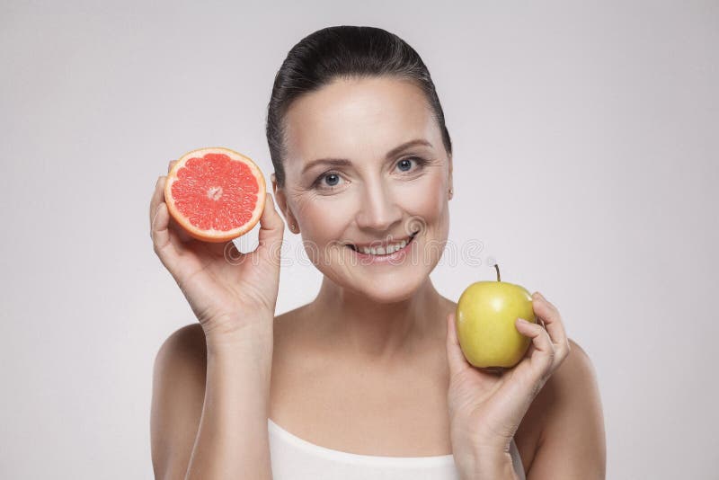 Portrait de femme âgée moyenne heureuse avec le sourire toothy de peau parfaite de visage, tenant le pamplemousse de tranche et l image stock Portrait de femme âgée moyenne heureuse avec le sourire toothy de peau parfaite de visage, tenant le pamplemousse de tranche et l image stock