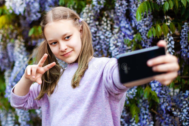 Portrait de fille du caucase de la préadolescence mignonne avec une queue de cheval en tenant le selfie contre l'arbre à fleurs de photos libres de droits