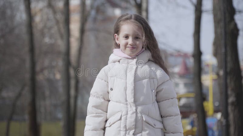 Portrait de fille du caucase de petite brune avec les cheveux bouclés face au parc en tant que personne inconnue traversant à l'av banque de vidéos