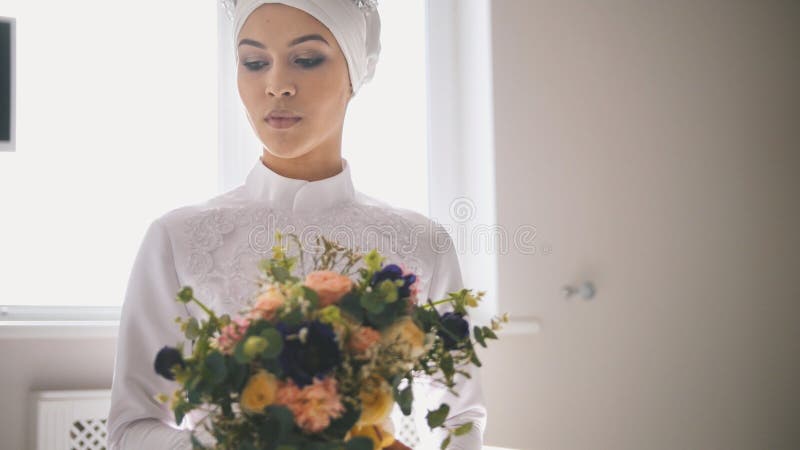 Portrait de jeune femme dans la robe de mariage islamique traditionnelle tenant le bouquet des fleurs images libres de droits Portrait de jeune femme dans la robe de mariage islamique traditionnelle tenant le bouquet des fleurs images libres de droits