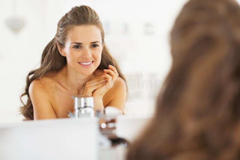 Portrait de jeune femme heureuse regardant dans le miroir dans la salle de bains images stock Portrait de jeune femme heureuse regardant dans le miroir dans la salle de bains images stock