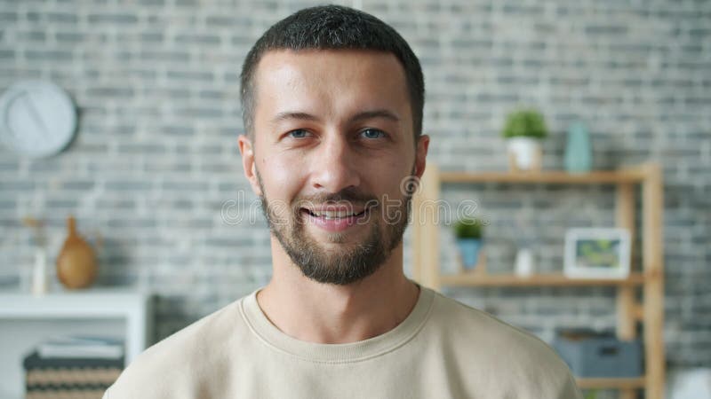 Portrait de jeune homme au mouvement lent, sérieux, souriant dans une maison cosy, regardant la caméra clips vidéos