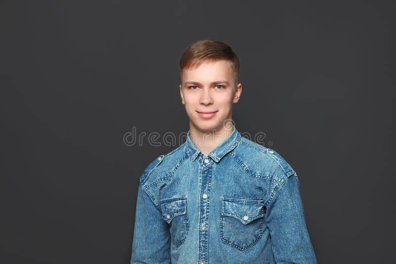 Portrait de jeune homme bel dans la chemise de jeans regardant l'appareil-photo au-dessus du fond gris-foncé Émotions et concept image stock Portrait de jeune homme bel dans la chemise de jeans regardant l'appareil-photo au-dessus du fond gris-foncé Émotions et concept image stock